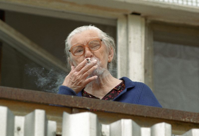 Престарелая женщина курит на балконе