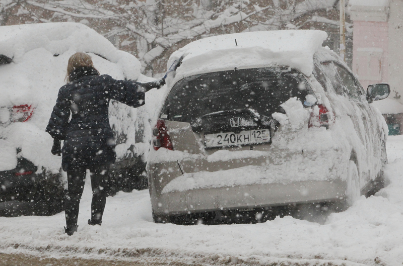 Женщина чистит от снега автомобиль во время снегопад