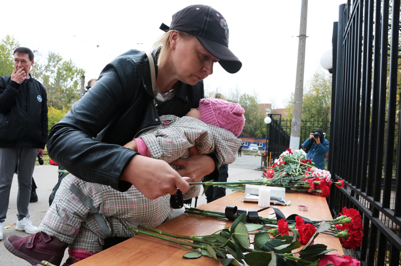 Женщина возлагает цветы в память о погибших в результате стрельбы в Пермском университете